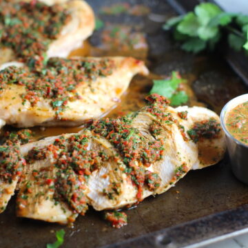 Chicken Chimichurri Rojo on a pan. It is broiled or grilled Chicken topped with a cool, fresh, tangy, and incredibly full-flavored! The Rojo comes from the addition of red pepper. All of the ingredients simply get blended in a food processor so it could not be easier! #chicken #chickenrecipes #chimichurri #easychicken #easydinners #dinner
