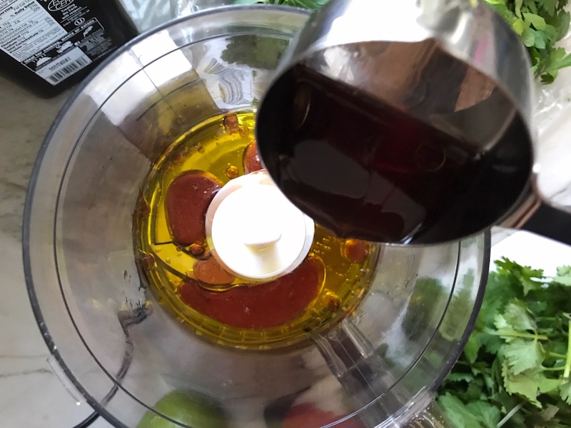 Adding Vinegar to oil in food processor for the Chicken Chimichurri Rojo. It is broiled or grilled Chicken topped with a cool, fresh, tangy, and incredibly full-flavored! The Rojo comes from the addition of red pepper. All of the ingredients simply get blended in a food processor so it could not be easier! #chicken #chickenrecipes #chimichurri #easychicken #easydinners #dinner