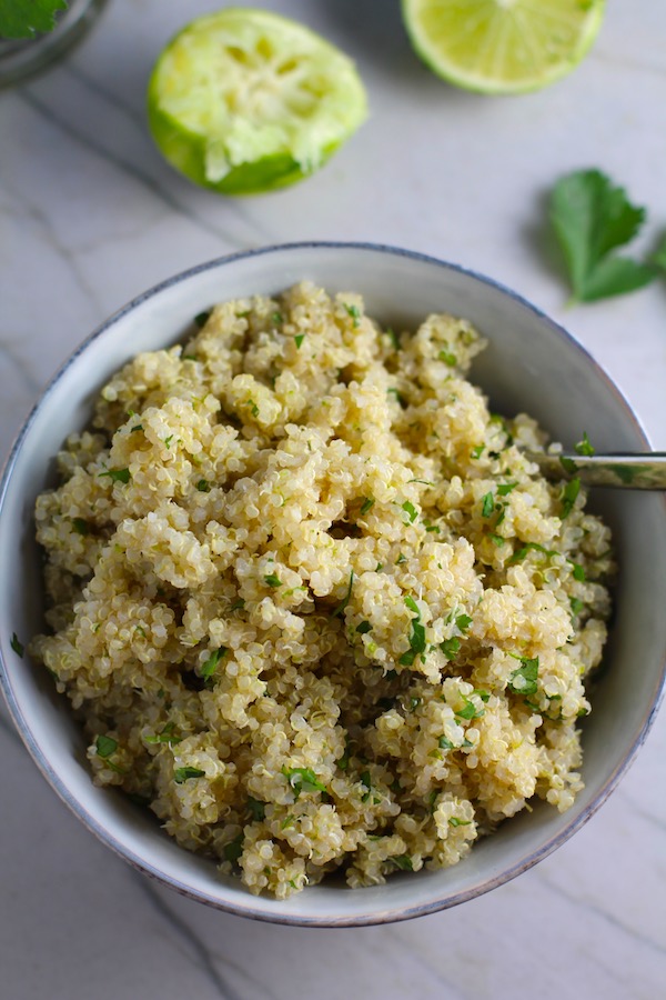 Cilantro Lime Quinoa in a bowl with spoon with lime and cilantro on counter. It's fluffy, nutty, citrusy, salty, and the perfect accompaniment for any protein or vegetable! With just a few simple ingredients, you can make this fantastic healthier alternative to rice. #quinoa #quinoarecipes #sides #healthyfood