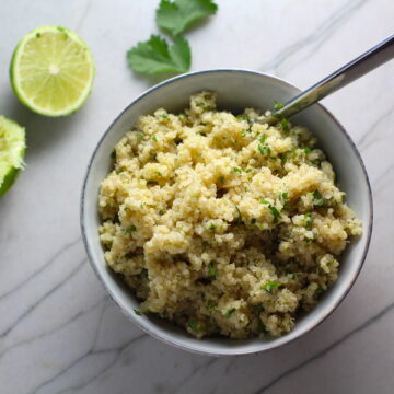 Cilantro Lime Quinoa in a bowl with spoon with lime and cilantro on counter. It's fluffy, nutty, citrusy, salty, and the perfect accompaniment for any protein or vegetable! With just a few simple ingredients, you can make this fantastic healthier alternative to rice. #quinoa #quinoarecipes #sides #healthyfood