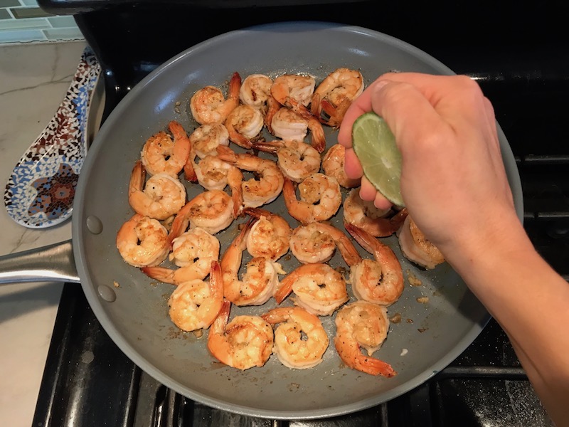 Squeezing lime over cooked shrimp in skillet for Garlic Lime Grilled Greek Shrimp with Tzatziki Sauce. The Shrimp is simply sauteed with minced garlic, olive oil, and lemon for big bold flavors. The Tzatziki Sauce is bright and cool with creamy yogurt with fresh cucumber, lime, garlic, and scallion. #shrimp #easydinner #dinner #seafoodrecipes #shrimprecipes