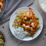 Garlic and Lime Shrimp with Tzatziki Sauce over Quinoa on plate. The Shrimp is simply sauteed with minced garlic, olive oil, and lemon for big bold flavors. The Tzatziki Sauce is bright and cool with creamy yogurt with fresh cucumber, lime, garlic, and scallion. #shrimp #easydinner #dinner #seafoodrecipes #shrimprecipes