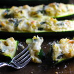 Fork with bite of Artichoke Spinach Stuffed Zucchini Recipe on a pan. Each fantastic bite gives you creamy artichoke, nutty cheesy Parmesan, spinach, and zucchini. Prepare entirely ahead, then bake 20 minutes and enjoy! #vegetarian #zucchini #stuffedzucchini #spinach #artichoke #springrecipes #healthyfood #healthydinner #healthyrecipes #glutenfree