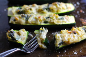 Fork with bite of Artichoke Spinach Stuffed Zucchini Recipe on a pan. Each fantastic bite gives you creamy artichoke, nutty cheesy Parmesan, spinach, and zucchini. Prepare entirely ahead, then bake 20 minutes and enjoy! #vegetarian #zucchini #stuffedzucchini #spinach #artichoke #springrecipes #healthyfood #healthydinner #healthyrecipes #glutenfree