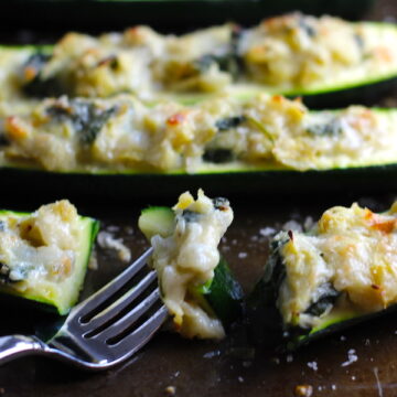 Fork with bite of Artichoke Spinach Stuffed Zucchini Recipe on a pan. Each fantastic bite gives you creamy artichoke, nutty cheesy Parmesan, spinach, and zucchini. Prepare entirely ahead, then bake 20 minutes and enjoy! #vegetarian #zucchini #stuffedzucchini #spinach #artichoke #springrecipes #healthyfood #healthydinner #healthyrecipes #glutenfree