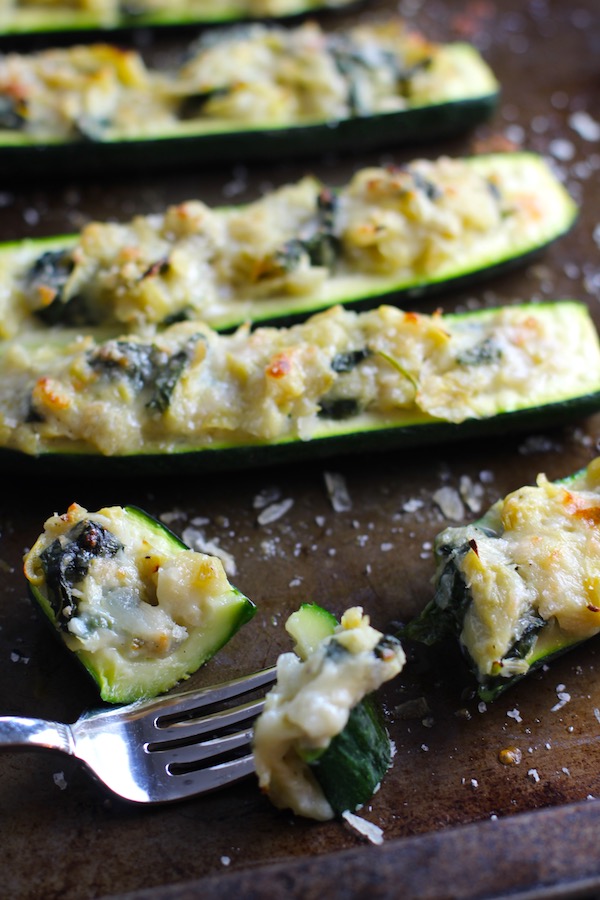 Fork with bite of Artichoke Spinach Stuffed Zucchini Recipe on a pan. Each fantastic bite gives you creamy artichoke, nutty cheesy Parmesan, spinach, and zucchini. Prepare entirely ahead, then bake 20 minutes and enjoy! #vegetarian #zucchini #stuffedzuchini #spinach #artichoke #springrecipes #healthyfood #healthydinner #healthyrecipes #glutenfree