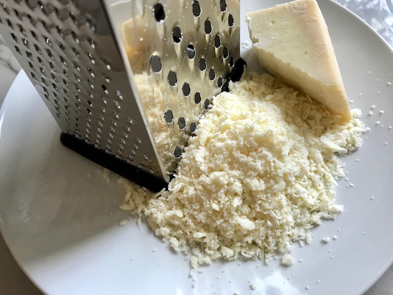 Grating Parmesan Cheese for Artichoke Spinach Stuffed Zucchini Recipe. Each fantastic bite gives you creamy artichoke, nutty cheesy Parmesan, spinach, and zucchini. Prepare entirely ahead, then bake 20 minutes and enjoy! #vegetarian #zucchini #stuffedzuchini #spinach #artichoke #springrecipes #healthyfood #healthydinner #healthyrecipes #glutenfree