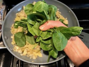 Adding to spinach leaves to onions cooking in pan for Artichoke Spinach Stuffed Zucchini Recipe. Each fantastic bite gives you creamy artichoke, nutty cheesy Parmesan, spinach, and zucchini. Prepare entirely ahead, then bake 20 minutes and enjoy! #vegetarian #zucchini #stuffedzuchini #spinach #artichoke #springrecipes #healthyfood #healthydinner #healthyrecipes #glutenfree
