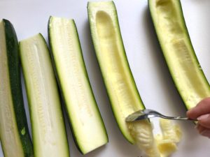 Spoon scooping seeds of zucchini half for Artichoke Spinach Stuffed Zucchini Recipe. Each fantastic bite gives you creamy artichoke, nutty cheesy Parmesan, spinach, and zucchini. Prepare entirely ahead, then bake 20 minutes and enjoy! #vegetarian #zucchini #stuffedzuchini #spinach #artichoke #springrecipes #healthyfood #healthydinner #healthyrecipes #glutenfree
