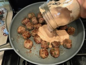 Adding Dill Cream Sauce to cooked meatballs in skillet for Meatballs in Cauliflower Dill Cream Sauce. #meatballs #swedishmeatballs #familydinner #easydinner #dinner #healthydinner