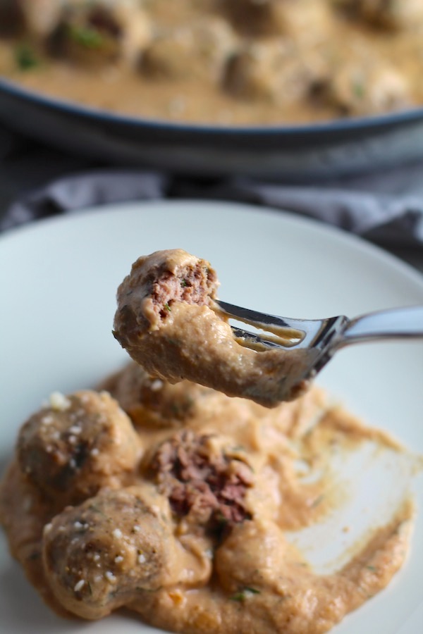 Meatballs in Cauliflower Dill Cream Sauce on plate with fork and skillet in background. The Meatballs are in a creamy cauliflower sauce with garlic, fresh dill, cream cheese, and tomato paste. #meatballs #swedishmeatballs #familydinner #easydinner #dinner #healthydinner