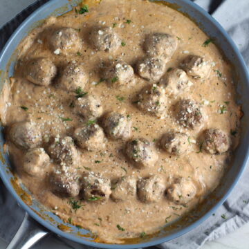 Meatballs in Cauliflower Dill Cream Sauce on plate with fork and skillet in background. The Meatballs are in a creamy cauliflower sauce with garlic, fresh dill, cream cheese, and tomato paste. #meatballs #swedishmeatballs #familydinner #easydinner #dinner #healthydinner
