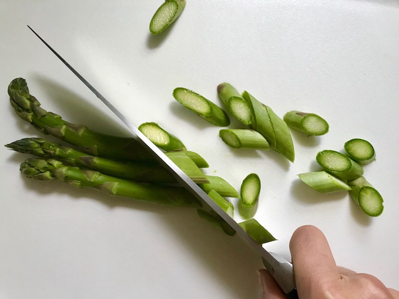 Knife cutting Asparagus on counter for Lemon Dill Sauce Chicken and Asparagus. It has chicken in a light and creamy sauce flavored with garlic, lemon and fresh dill. It's loaded with fresh asparagus. #springrecipes #dinner #easydinner #healthydinner #lemon #asparagus #chicken #glutenfree #easyrecipes