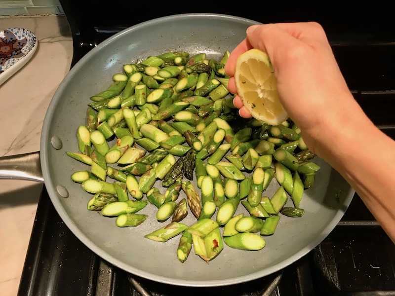 Cut asparagus cooking in pan with hand squeezing lemon over for Lemon Dill Sauce Chicken and Asparagus. It has chicken in a light and creamy sauce flavored with garlic, lemon and fresh dill. It's loaded with fresh asparagus. #springrecipes #dinner #easydinner #healthydinner #lemon #asparagus #chicken #glutenfree #easyrecipes