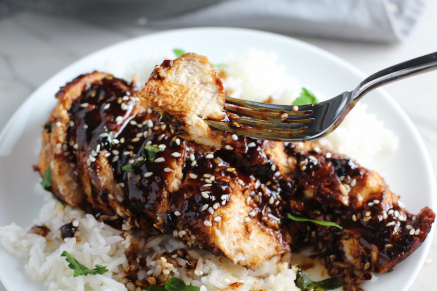 Bite of Sesame Sweet Chili Chicken on a fork over more sliced on a plate with rice. It is slightly sweet, tangy, savory, nutty, with a touch of heat. You can prepare it days ahead, it takes just minutes to prepare, minutes to cook, and everyone will love it!! #chicken #marinades #easydinner #easychicken #chickenrecipes #easysauces #healthydinner #healthyfood #healthyrecipes