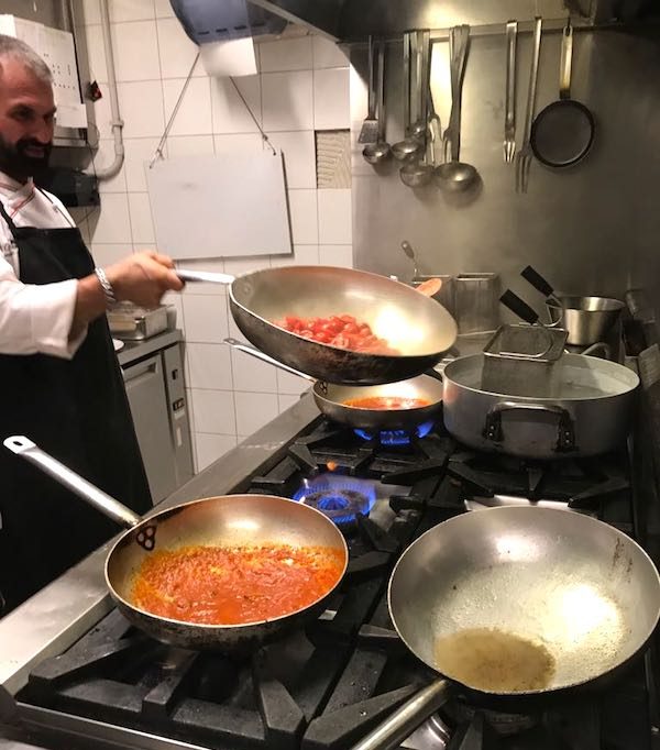Cooking Class in Italy with chef flipping cherry tomatoes in pan. Inspiration for Chicken with Cherry Tomatoes pasta recipe.