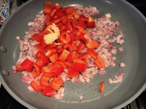 Diced onion, red pepper, and garlic in skillet cooking for Skillet Eggs in Spicy Tomato Pepper Sauce with Manchego Cheese. With a smoky, spicy, thick, and luscious red pepper tomato sauce. #eggs #huevosrancheros #tomatosauce #easydinner #brunch #shakshuka
