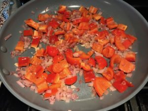 Diced onion, red pepper, and garlic in skillet cooking for Skillet Eggs in Spicy Tomato Pepper Sauce with Manchego Cheese. With a smoky, spicy, thick, and luscious red pepper tomato sauce. #eggs #huevosrancheros #tomatosauce #easydinner #brunch #shakshuka