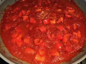 Spices, tomato sauce, diced onion, red pepper, and garlic in skillet cooking for Skillet Eggs in Spicy Tomato Pepper Sauce with Manchego Cheese. With a smoky, spicy, thick, and luscious red pepper tomato sauce. #eggs #huevosrancheros #tomatosauce #easydinner #brunch #shakshuka