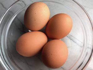 4 Brown Eggs in a clear glass bowl for Skillet Eggs in Spicy Tomato Pepper Sauce with Manchego Cheese. With a smoky, spicy, thick, and luscious red pepper tomato sauce. #eggs #huevosrancheros #tomatosauce #easydinner #brunch #shakshuka