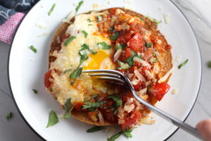 Skillet Eggs in Spicy Tomato Pepper Sauce with Manchego Cheese served over a crispy corn tortilla with skillet in back. With a smoky, spicy, thick, and luscious red pepper tomato sauce. #eggs #huevosrancheros #tomatosauce #easydinner #brunch #shakshuka