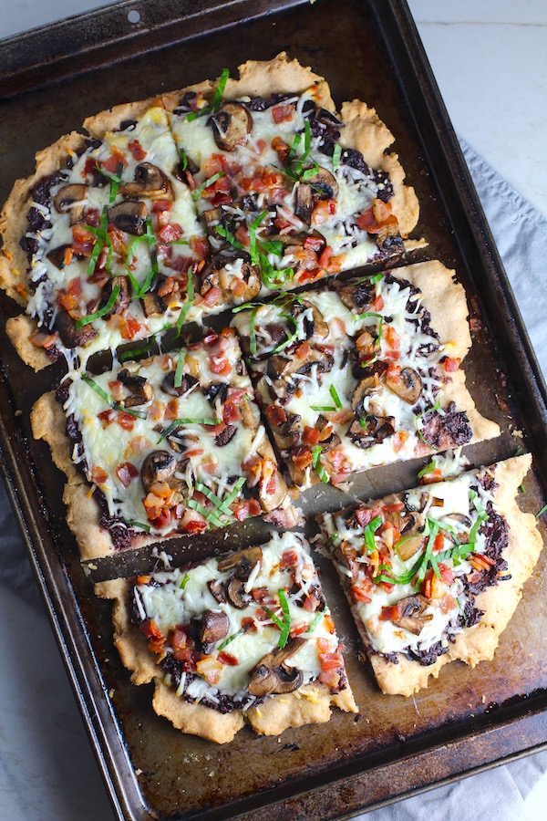 Flatbread cut into 3 pieces on a pan with a crispy gluten free crust, salty and briny Olive Tapenade, creamy mozzarella, earthy and meaty mushrooms, peppery pancetta, and fresh basil. #flatbread #pizza #olives #tapenade #mediterranean #easydinner #dinner