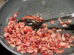 Scooping pancetta from skillet with slotted spoon for Olive & Pancetta Flatbread with mozzarella, mushrooms, and fresh basil. #flatbread #pizza #olives #tapenade #mediterranean #easydinner #dinner