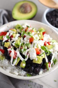 Black Bean Taco Bowl with rice, smoky black beans, avocado, salty Cotija cheese, sour cream, fresh tomato, and bright cilantro. This Black Bean Taco Bowl Bar lets everyone fills their bowl with any of the toppings they want! Perfect for kids. #tacos #tacobowls #healthyfood #dinner #healthydinner #familydinner #kidsdinner #blackbeans #vegetarian