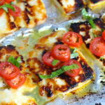 Grilled Halloumi Cheese & Tomato Salad on pan. It's insanely delicious! Grilled Halloumi has a strong savory and salty flavor that is slightly creamy and incredibly addictive. Paired with my simple Tomato and Basil salad, each bite is simply heaven. #halloumi #appetizers #salads #grilling #summerfood