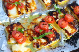 Grilled Halloumi Cheese & Tomato Salad on pan. It's insanely delicious! Grilled Halloumi has a strong savory and salty flavor that is slightly creamy and incredibly addictive. Paired with my simple Tomato and Basil salad, each bite is simply heaven. #halloumi #appetizers #salads #grilling #summerfood