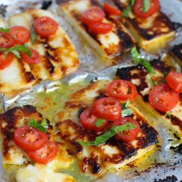 Grilled Halloumi Cheese & Tomato Salad on pan. It's insanely delicious! Grilled Halloumi has a strong savory and salty flavor that is slightly creamy and incredibly addictive. Paired with my simple Tomato and Basil salad, each bite is simply heaven. #halloumi #appetizers #salads #grilling #summerfood