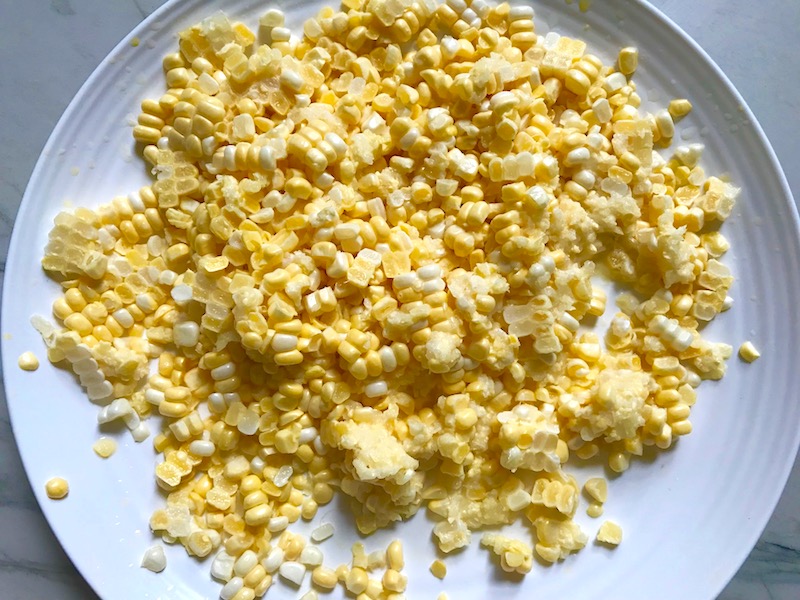 Kernels cut from a cob of corn for Chilled Golden Corn Soup with Turmeric. Scallions on top for garnish. It's thick, creamy, silky and delicious. The entire family will love this easy stovetop corn soup! #summerfood #cornsoup #corn #vegetarian #vegetablerecipes #sides