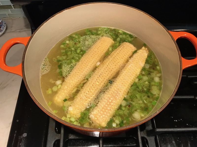 Corn cobs in broth with sliced scallions in a soup pot for Chilled Golden Corn Soup with Turmeric. Scallions on top for garnish. It's thick, creamy, silky and delicious. The entire family will love this easy stovetop corn soup! #summerfood #cornsoup #corn #vegetarian #vegetablerecipes #sides