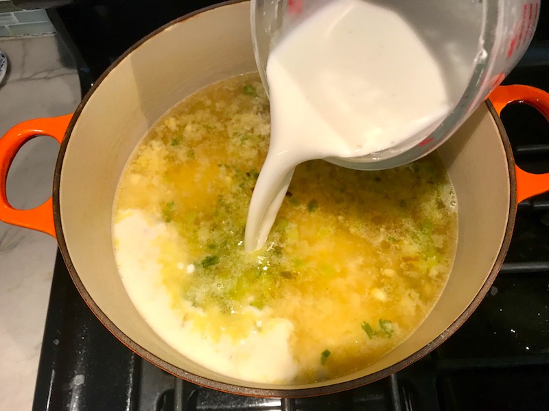 Adding Cornstarch slurry to corn soup in pot for Chilled Golden Corn Soup with Turmeric. Scallions on top for garnish. It's thick, creamy, silky and delicious. The entire family will love this easy stovetop corn soup! #summerfood #cornsoup #corn #vegetarian #vegetablerecipes #sides