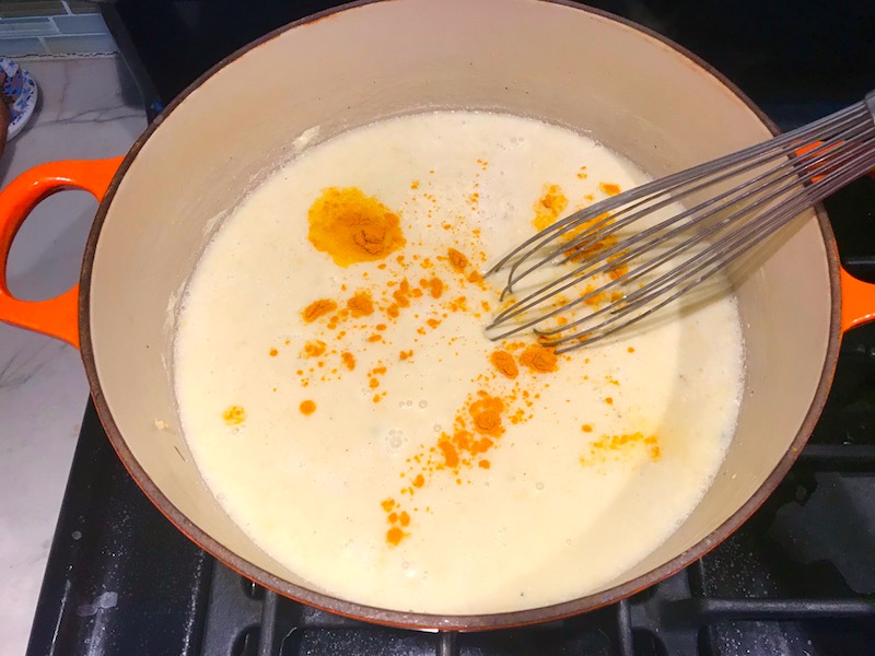 Whisking turmeric and half and half into corn soup in pot for Chilled Golden Corn Soup with Turmeric. Scallions on top for garnish. It's thick, creamy, silky and delicious. The entire family will love this easy stovetop corn soup! #summerfood #cornsoup #corn #vegetarian #vegetablerecipes #sides