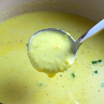 Closeup of Chilled Golden Corn Soup in a pot with a ladle scooping soup up. Scallions on top for garnish. It's thick, creamy, silky and delicious.  The entire family will love this easy stovetop corn soup! #summerfood #cornsoup #corn #vegetarian #vegetablerecipes #sides
