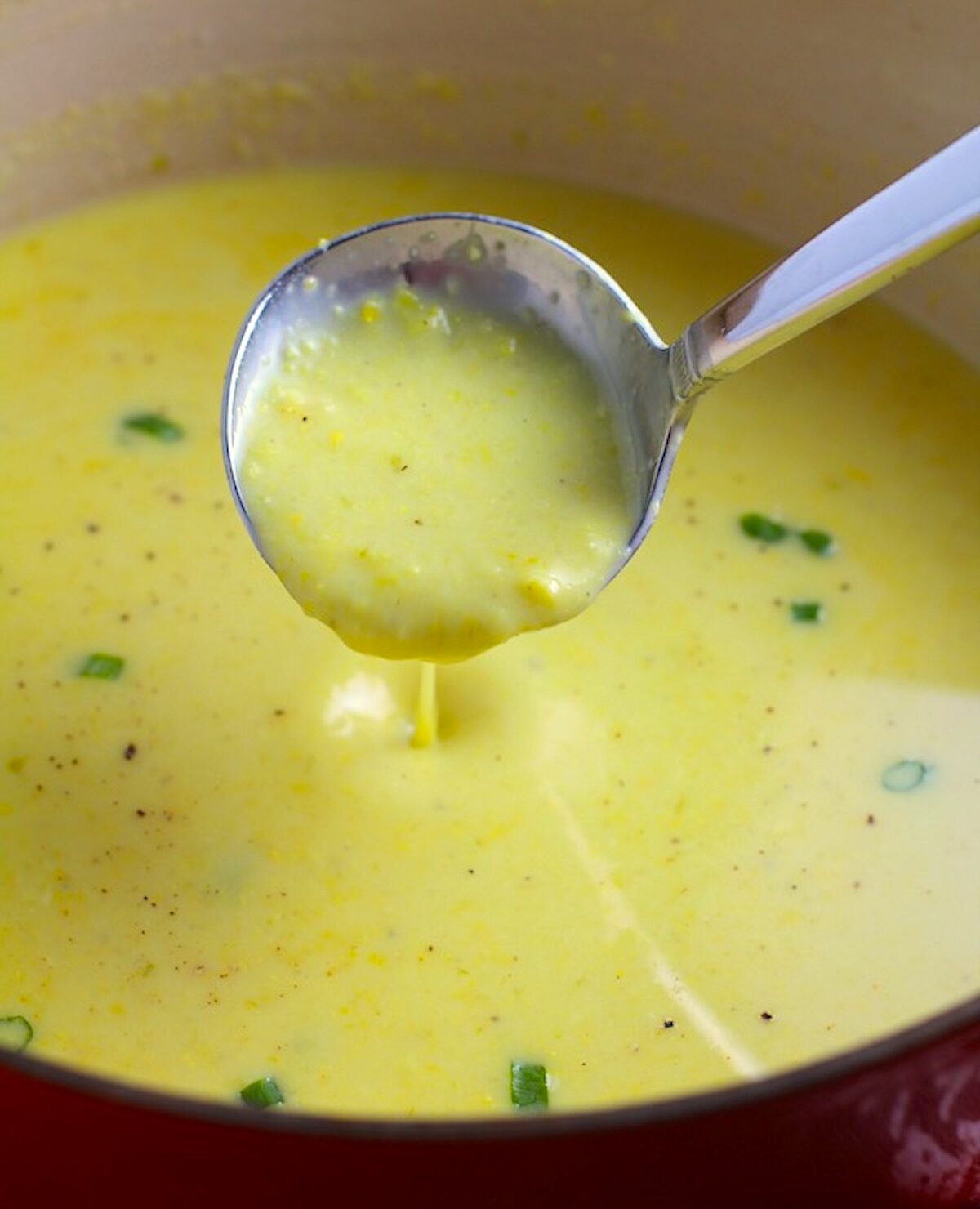 Gluten free Corn Chowder in a pot with a ladle scooping some up and scallions on top as garnish.
