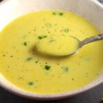Gluten free Corn Chowder in a bowl with a spoon scooping up some and scallions on top as garnish.