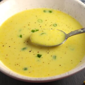 Gluten free Corn Chowder in a bowl with a spoon scooping up some and scallions on top as garnish.