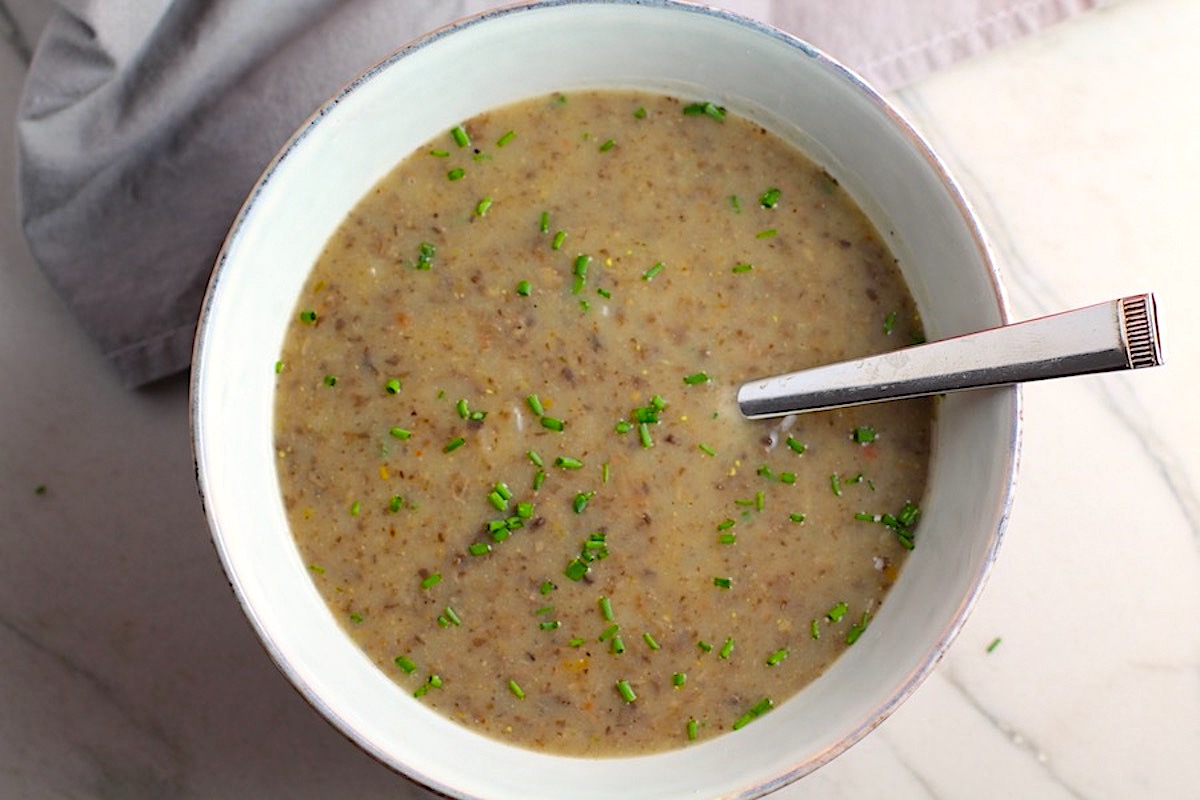 Gluten Free Cream of Mushroom Soup in a bowl with spoon filled with earthy mushrooms, aeromatic onions, flavorful oregano, and bright chives.