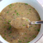 Gluten Free Cream of Mushroom Soup in a bowl with spoon filled with earthy mushrooms, aeromatic onions, flavorful oregano, and bright chives.
