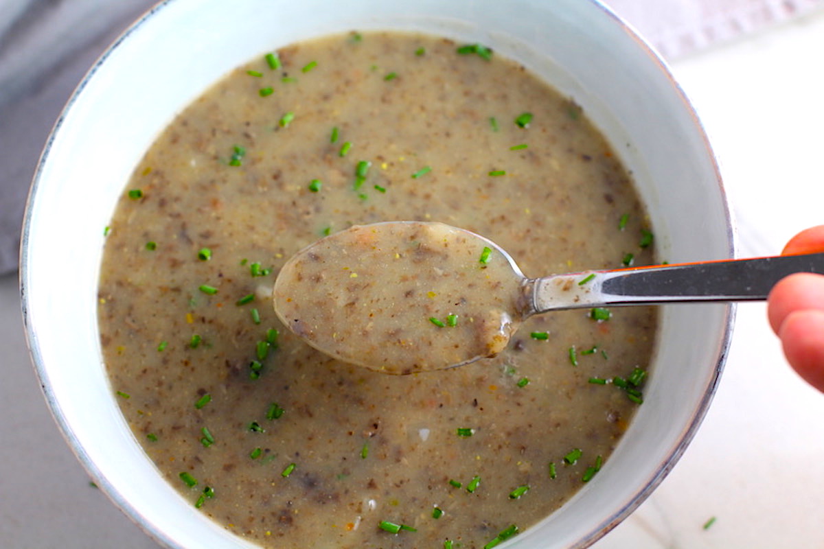 Gluten Free Cream of Mushroom Soup in a bowl with spoon filled with earthy mushrooms, aeromatic onions, flavorful oregano, and bright chives.