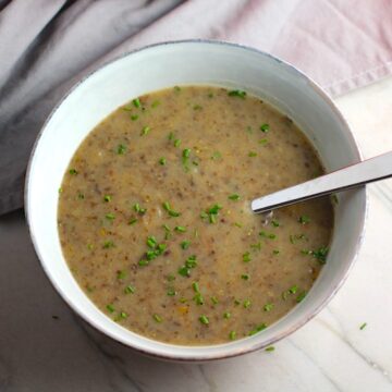 Gluten Free Cream of Mushroom Soup in a bowl with spoon filled with earthy mushrooms, aeromatic onions, flavorful oregano, and bright chives.