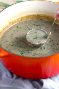 Thick & Creamy Healthy Mushroom Soup in a pot with ladle filled with earthy mushrooms, aeromatic onions, flavorful oregano, and bright chives.