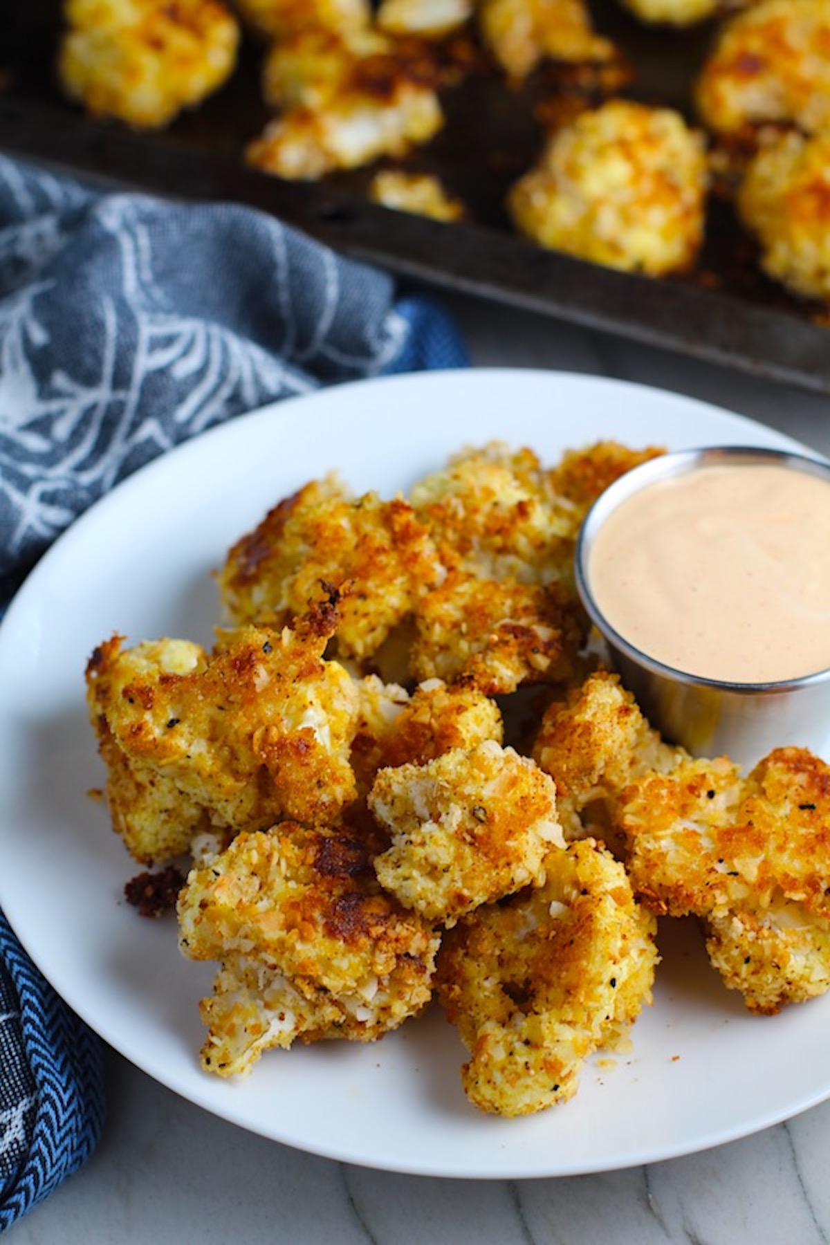 Baked Breaded Cauliflower Recipe on plate with Sriracha Mayo dipping sauce. They have a slightly sweet and salty crunch outside from the shredded coconut and panko mixture. The inside is soft and creamy. Dip in the Sriracha Mayo.