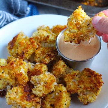 Breaded Cauliflower Recipe on plate with Sriracha Mayo dipping sauce.  They have a slightly sweet and salty crunch outside from the shredded coconut and panko mixture.  The inside is soft and creamy.  Dip in the Sriracha Mayo. 