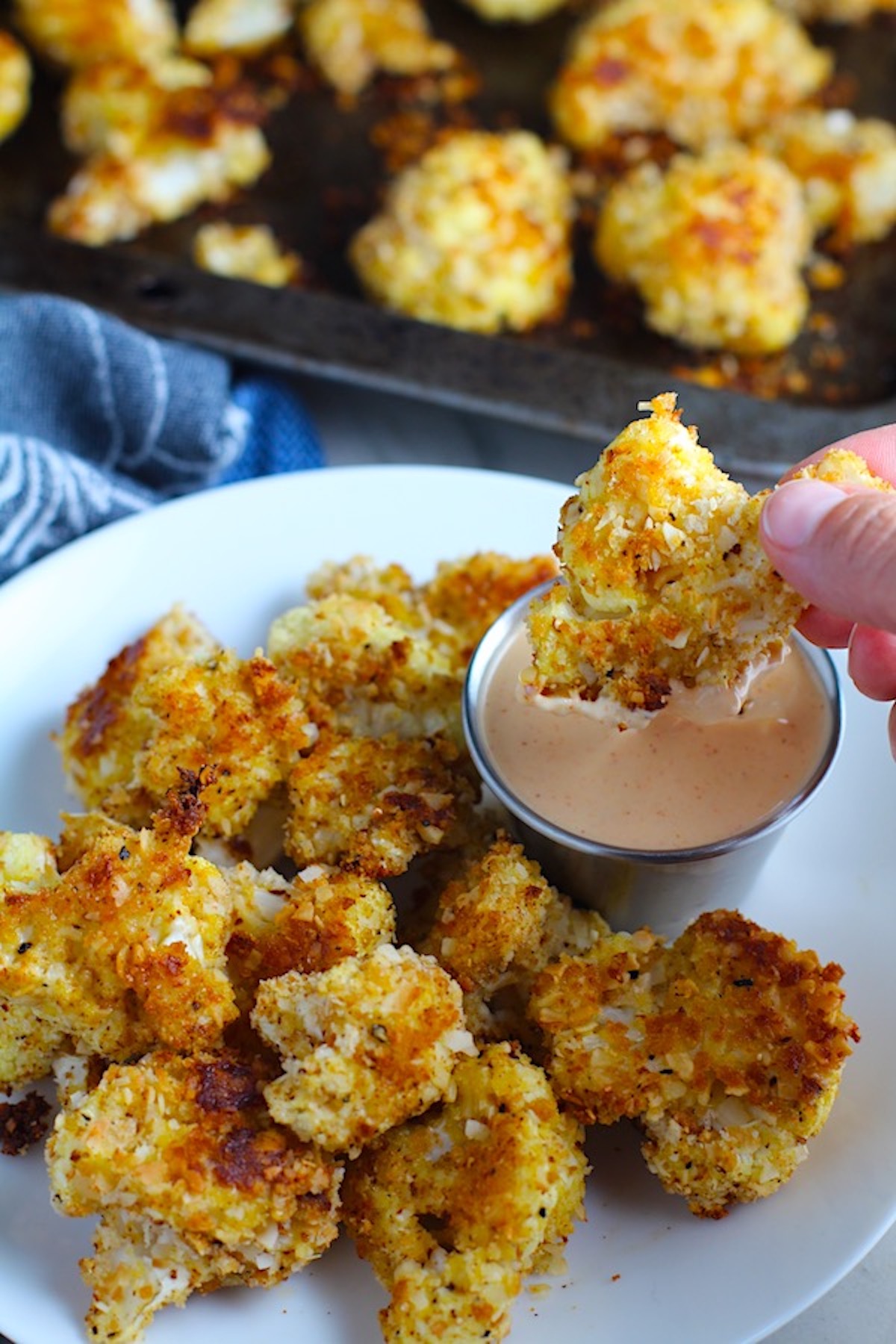 Breaded Cauliflower Recipe on plate with Sriracha Mayo dipping sauce. They have a slightly sweet and salty crunch outside from the shredded coconut and panko mixture. The inside is soft and creamy. Dip in the Sriracha Mayo.