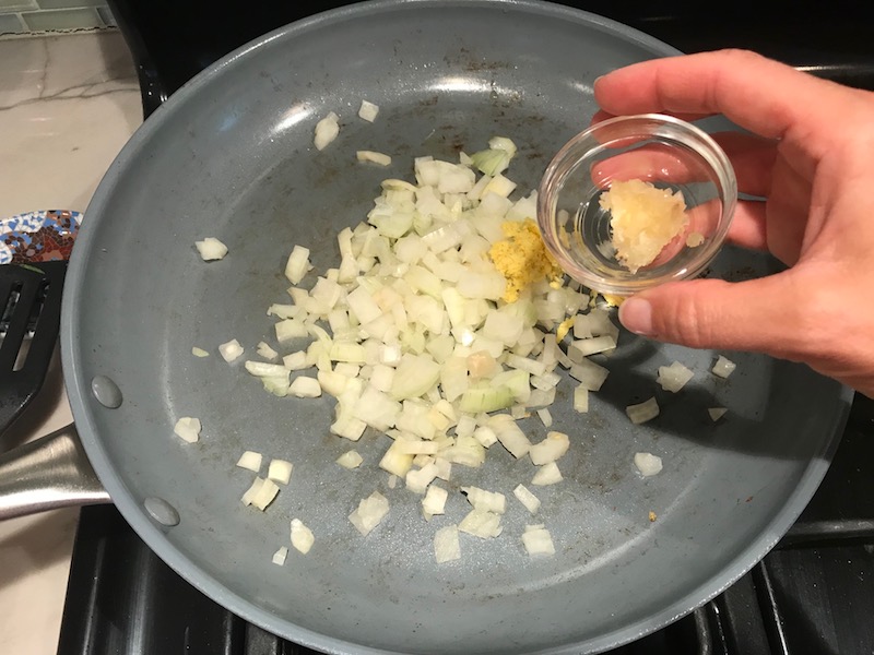 Adding garlic to onions and ginger in pan for Family Coconut Curry. The sauce has onion, coconut milk, ginger, garlic, and warm Indian Curry spices.
