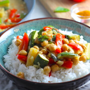 Family Zucchini Chickpea Curry over rice in a bowl with red bell pepper, zucchini, onion, coconut milk, and warm Indian Curry spices.
