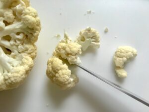 Knife cutting cauliflower for Baked Coconut Crispy Cauliflower Bites. They have a slightly sweet and salty crunch outside from the shredded coconut and panko mixture. The inside is soft and creamy. Dip in the Sriracha Mayo. Baked, not fried, so healthy! Easy to make, easy to eat! #cauliflowerrecipes #healthyrecipes #sidedishes #appetizers #healthysnacks